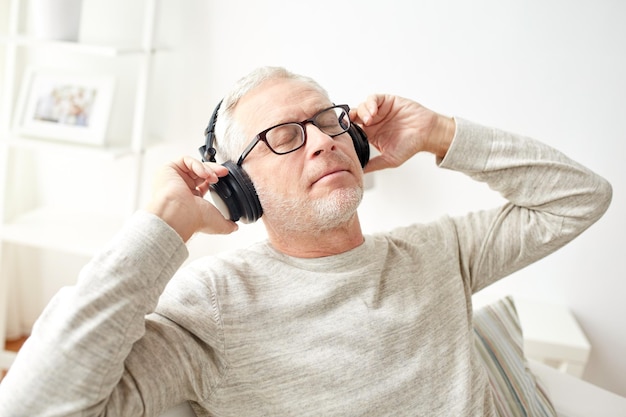 concetto di tecnologia, persone e stile di vita - uomo anziano felice in cuffia che ascolta musica a casa