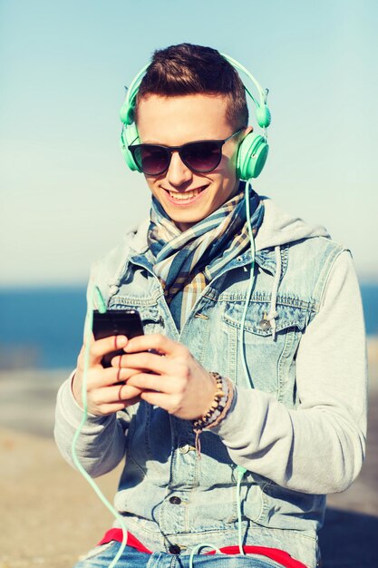 concetto di tecnologia, stile di vita e persone - giovane sorridente o adolescente in cuffie con smartphone che ascolta musica all'aperto