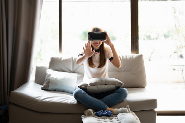 Concetto di tecnologiagiocodivertimento e personedonna asiatica che si gode gli occhiali per realtà virtuale mentre ci si rilassa in soggiornoFelice ragazzo con auricolare VR che gioca al videogioco a casa