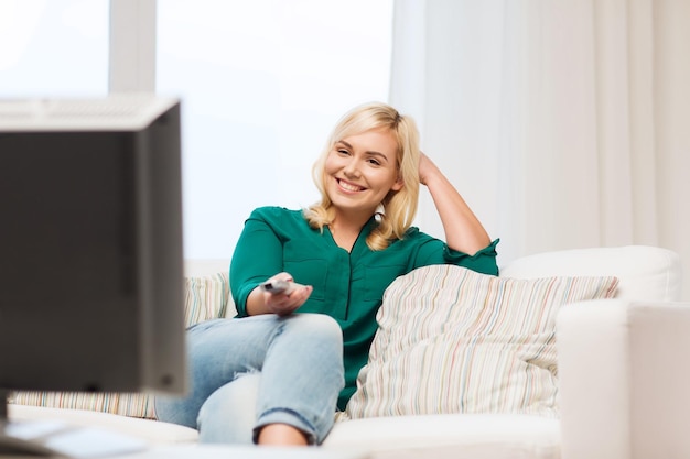 concetto di televisione, tempo libero e persone - donna sorridente seduta sul divano con telecomando e guardare la tv a casa