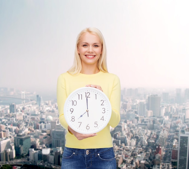 concetto di tempo, istruzione e persone - giovane donna sorridente con orologio da parete che mostra 8