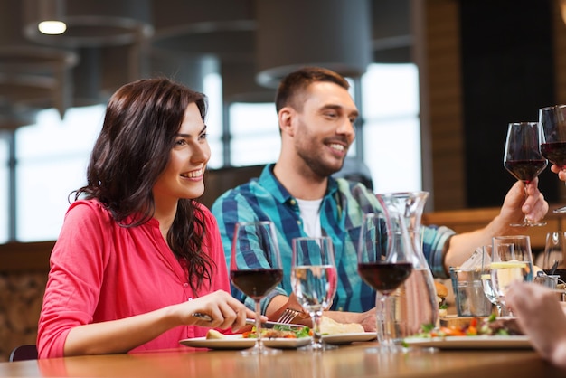 concetto di tempo libero, celebrazione, cibo e bevande, persone e vacanze - coppia felice e amici che tintinnano bicchieri di vino al ristorante