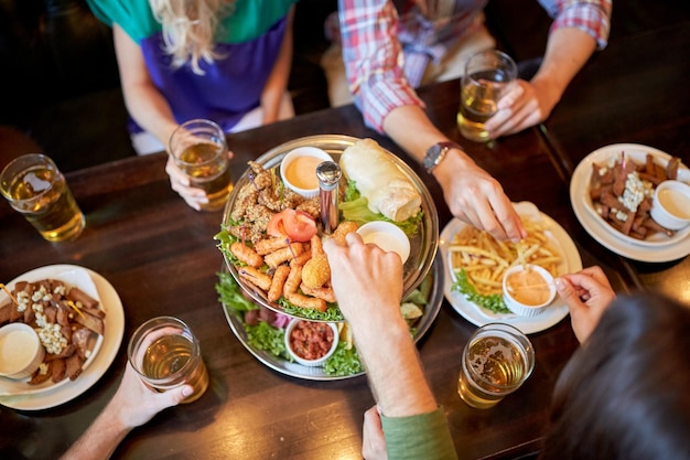 concetto di tempo libero, cibo, bevande, persone e vacanze - amici che mangiano snack e bevono birra al bar o al pub