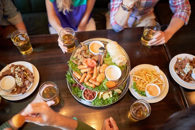 concetto di tempo libero, cibo, bevande, persone e vacanze - amici che mangiano snack e bevono birra al bar o al pub