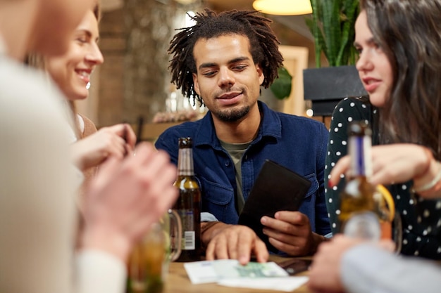 concetto di tempo libero, persone e vacanze - amici felici con bevande, denaro e conto al bar o al caffè