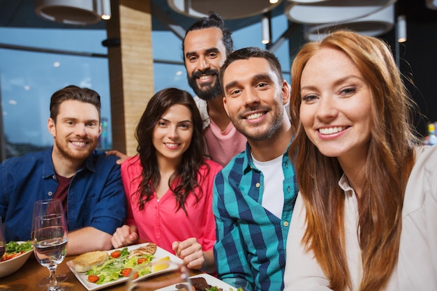 concetto di tempo libero, tecnologia, amicizia, persone e vacanze - amici felici che cenano e si fanno selfie con lo smartphone al ristorante