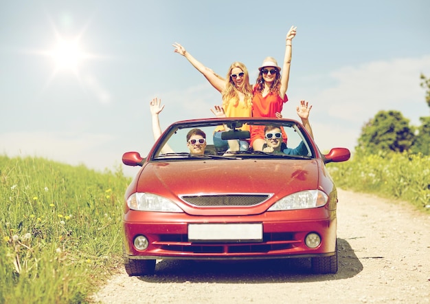 concetto di tempo libero, viaggio su strada, viaggio e persone - amici felici che guidano in auto cabriolet in campagna e agitano le mani