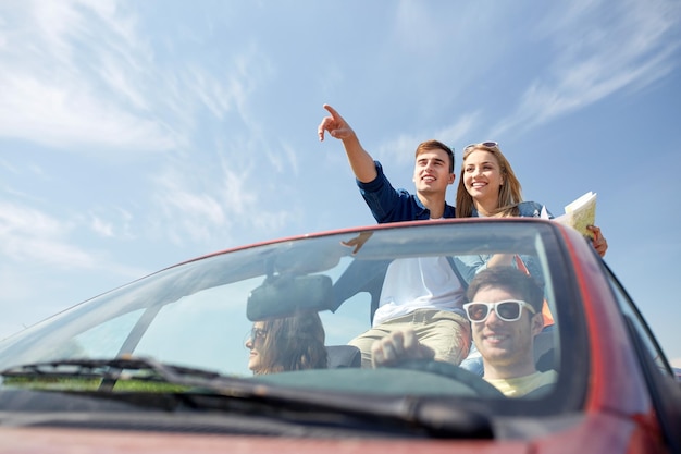 concetto di tempo libero, viaggio su strada, viaggio e persone - amici felici con la mappa che guidano in auto cabriolet lungo la strada di campagna e puntano il dito verso qualcosa davanti