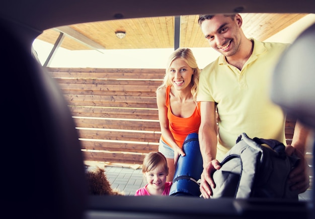 concetto di trasporto, tempo libero, viaggi, viaggio su strada e persone - famiglia felice che imballa le cose nel parcheggio dell'auto a casa