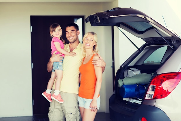 concetto di trasporto, tempo libero, viaggio su strada, viaggi e persone - famiglia felice con la bambina che imballa le cose auto berlina nel parcheggio di casa