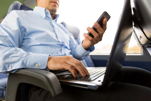 concetto di trasporto, turismo, viaggio d'affari e persone - primo piano dell'uomo con smartphone e laptop in autobus da viaggio
