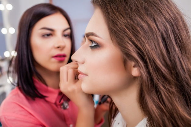 Concetto di trucco e di bellezza - ritratto del primo piano di bella donna che ottiene trucco professionale con la spazzola