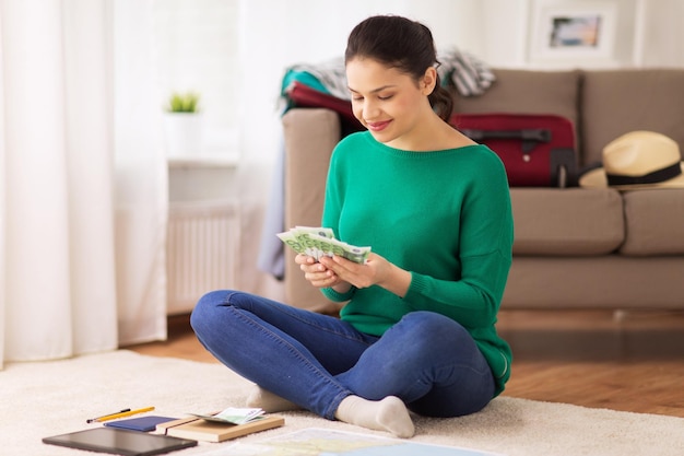 concetto di turismo, viaggi, finanze e persone - giovane donna felice con soldi, computer tablet pc e mappa a casa