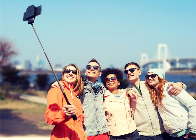 concetto di turismo, viaggi, persone, tempo libero e tecnologia - gruppo di amici adolescenti sorridenti che prendono selfie con smartphone e monopiede sul ponte arcobaleno nella città di tokyo