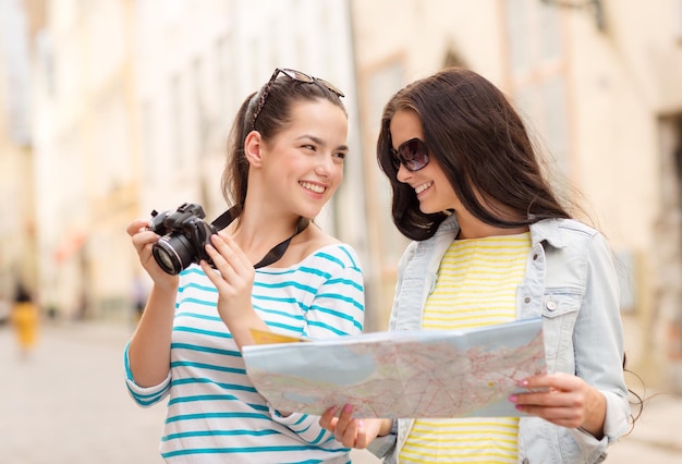 concetto di turismo, viaggi, tempo libero, vacanze e amicizia - due adolescenti sorridenti con mappa e fotocamera all'aperto