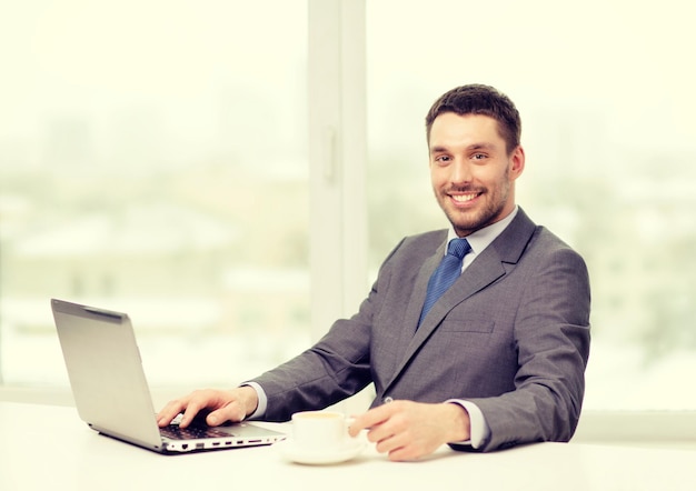 concetto di ufficio, affari, tecnologia e internet - uomo d'affari sorridente con computer portatile e caffè in ufficio