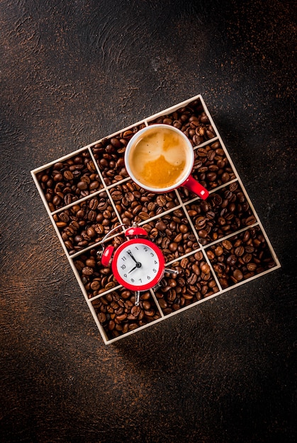 Concetto di un allegro, buon inizio di giornata, caffè mattutino. Sfondo arrugginito scuro con chicchi di caffè, una sveglia e una tazza di caffè. Vista dall'alto copia spazio