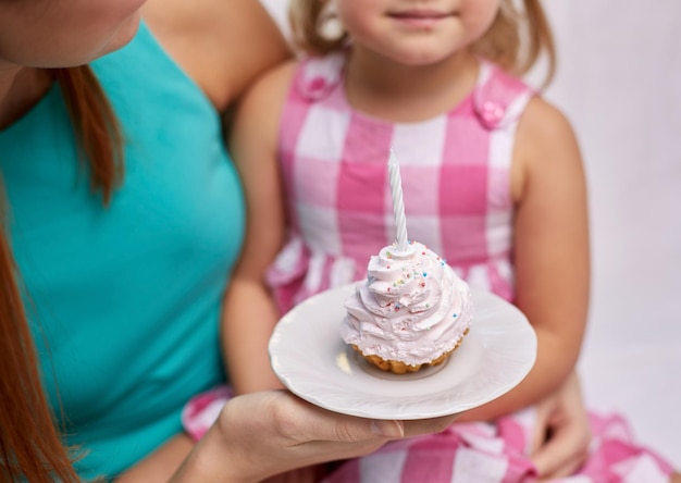 concetto di vacanza, celebrazione, famiglia, compleanno e persone - madre felice e bambina che tengono cupcake con la candela