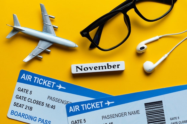 Concetto di vacanza di novembre accanto ai biglietti e al modello dell'aeroplano su fondo giallo.