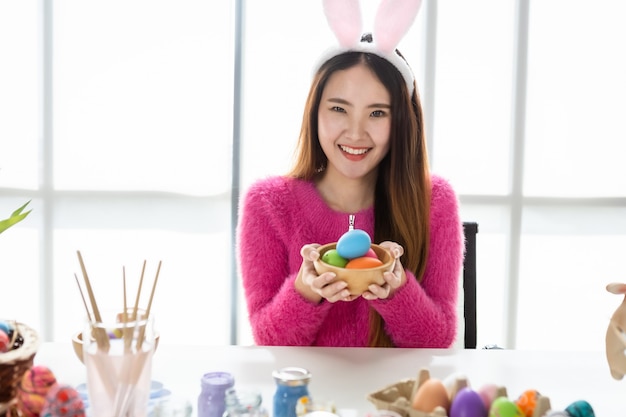 Concetto di vacanza di Pasqua, spettacolo di una giovane donna asiatica felice che tiene in mano un cesto con uova di Pasqua colorate sullo sfondo della stanza bianca