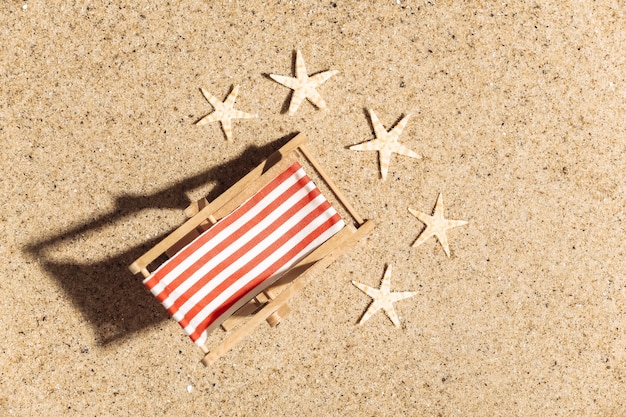 Concetto di vacanza di viaggio di estate spiaggia. Mini sedia a sdraio da spiaggia sulla sabbia con stelle marine in una luminosa giornata di sole.