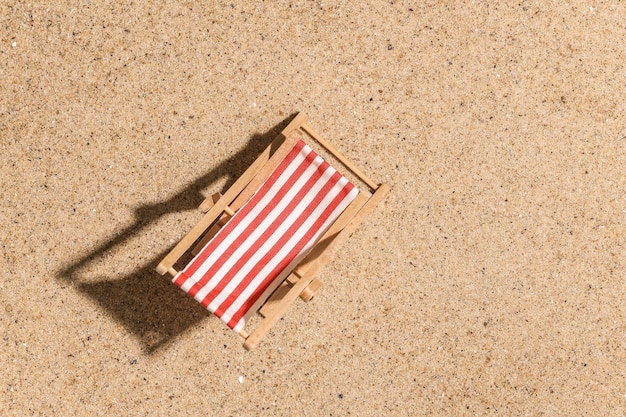 Concetto di vacanza di viaggio di estate spiaggia. Mini sedia a sdraio da spiaggia sulla sabbia in una luminosa giornata di sole. Vista dall'alto