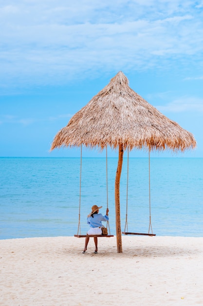 Concetto di vacanza estiva Giovane donna che indossa un abito blu elegante e cappello di paglia con un cielo blu sulla spiaggia.