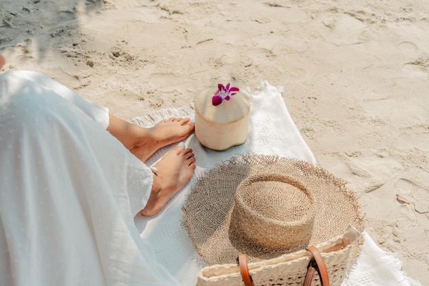 Concetto di vacanza estiva Piedi e cappello di paglia con noci di cocco sulla sabbia sulla spiaggia