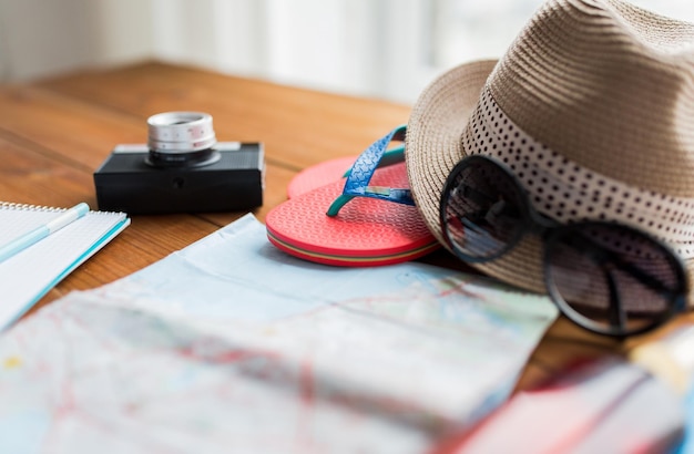 concetto di vacanza estiva, turismo e oggetti - primo piano della mappa di viaggio, infradito, cappello e macchina fotografica sul tavolo di legno a casa
