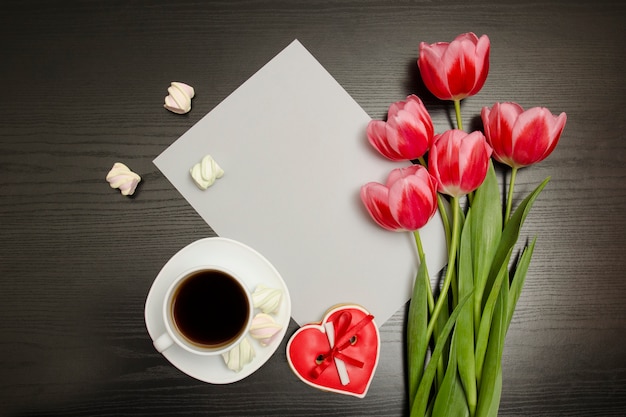 Concetto di vacanza. Mazzo di tulipani rosa, una tazza di caffè, biscotti a forma di cuore rossi con una nota