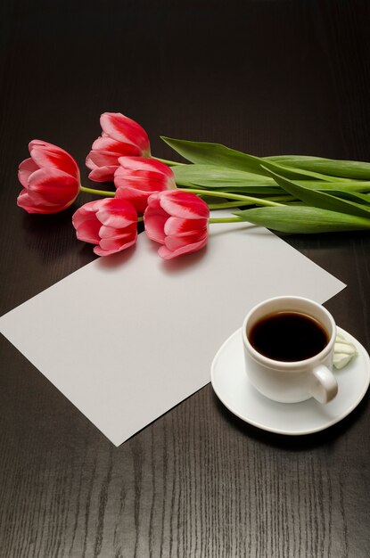 Concetto di vacanza. Mazzo di tulipani rosa, una tazza di caffè e un foglio di carta