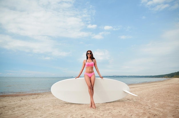 concetto di vacanza, surf, sport acquatici e persone - giovane donna in costume da bagno con tavola da surf, windsurf o paddle board sulla spiaggia estiva