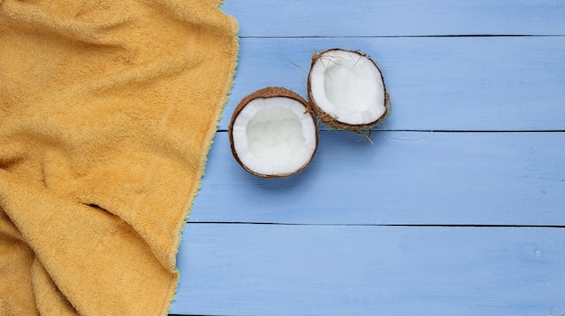 Concetto di vacanza tropicale minimalista. Metà della noce di cocco, tovagliolo su un legno blu