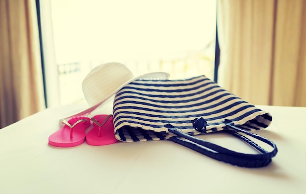 concetto di vacanza, vacanza e viaggio - primo piano di borsa da spiaggia, cappello di paglia e infradito sul letto dell'hotel