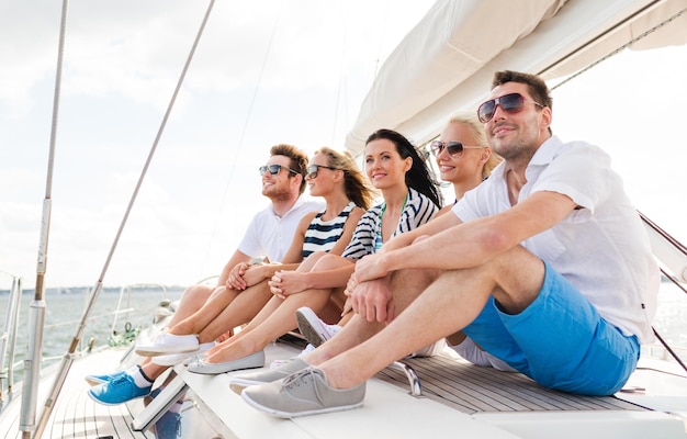 concetto di vacanza, viaggio, mare, amicizia e persone - amici sorridenti seduti sul ponte dello yacht