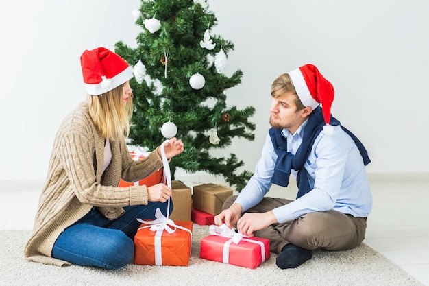 Concetto di vacanze - coppia dolce che apre i regali di Natale, seduta in soggiorno.