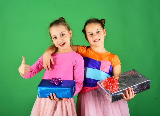 Concetto di vacanze di Natale I bambini aprono i regali per Natale Ragazze con facce sorridenti abbracciano con regali su sfondo verde Sorelle con scatole regalo avvolte per le vacanze mostrano pollice in alto