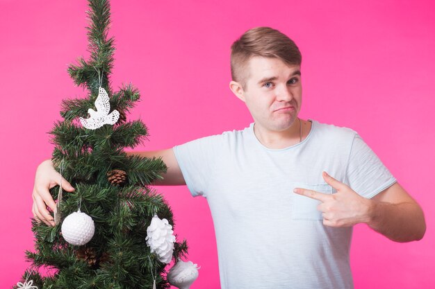 Concetto di vacanze e persone - Uomo felice con albero di Natale sulla parete rosa.