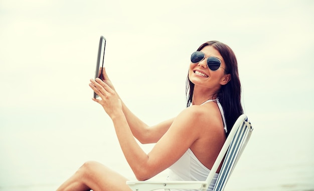 concetto di vacanze estive, turismo, viaggi, vacanze e persone - giovane donna sorridente con computer tablet pc che prende il sole in salotto o sedia pieghevole sulla spiaggia