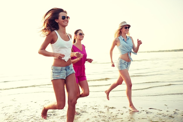 concetto di vacanze estive, vacanze, viaggi e persone - gruppo di giovani donne sorridenti in occhiali da sole e abiti casual che corrono sulla spiaggia