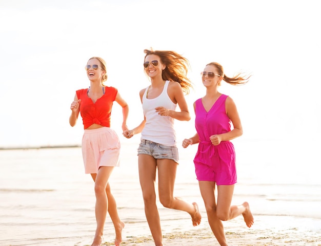 concetto di vacanze estive, vacanze, viaggi e persone - gruppo di giovani donne sorridenti in occhiali da sole e abiti casual che corrono sulla spiaggia