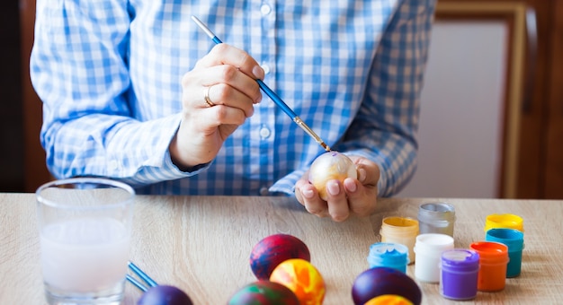 Concetto di vacanze, fatto a mano e creazione. La giovane donna felice attinge l'uovo di Pasqua, primo piano.