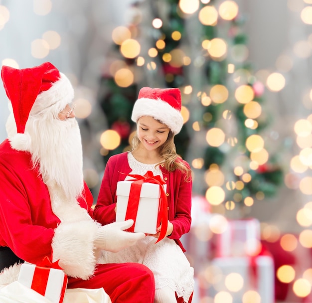 concetto di vacanze, infanzia e persone - bambina sorridente con Babbo Natale e regali su sfondo di luci di luci dell'albero di Natale