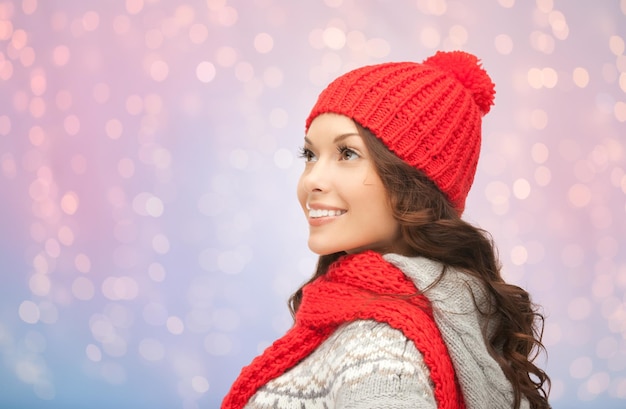 concetto di vacanze invernali, natale e persone - giovane donna sorridente con cappello rosso e sciarpa su sfondo di luci di quarzo rosa e serenità