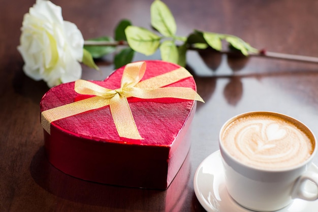 concetto di vacanze, san valentino, amore e bevande - primo piano di confezione regalo, tazza di caffè e fiore sul tavolo