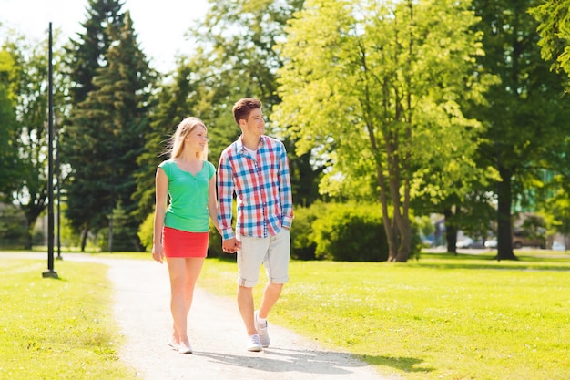 concetto di vacanze, vacanze, amore e amicizia - coppia sorridente che cammina e si tiene per mano nel parco