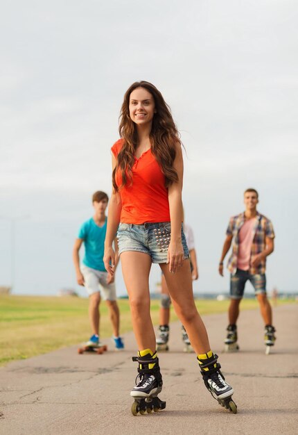 concetto di vacanze, vacanze, amore e amicizia - gruppo di adolescenti sorridenti con pattini a rotelle e skateboard all'aperto