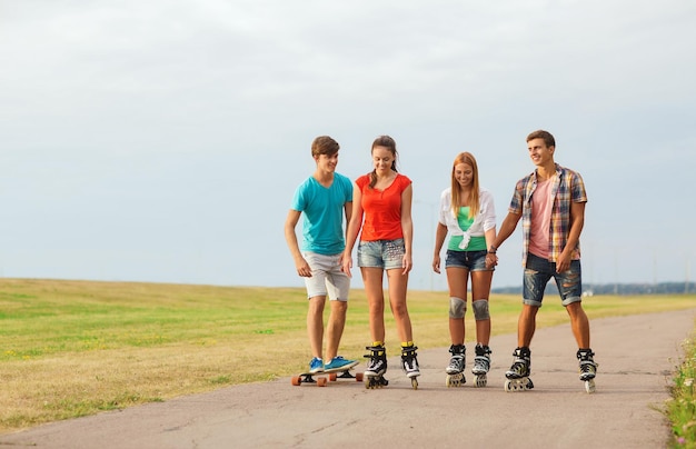 concetto di vacanze, vacanze, amore e amicizia - gruppo di adolescenti sorridenti con pattini a rotelle e skateboard all'aperto