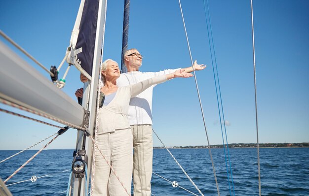 concetto di vela, età, turismo, viaggi e persone - coppia senior felice che si gode la libertà sulla barca a vela o sul ponte dello yacht che galleggia nel mare