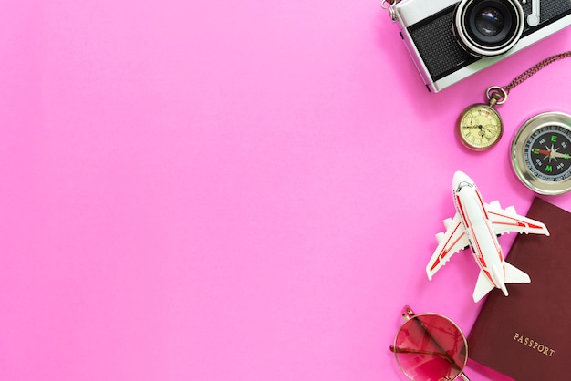 Concetto di viaggi ed orari estivi. Disposizione piana degli accessori e macchina fotografica su fondo rosa.